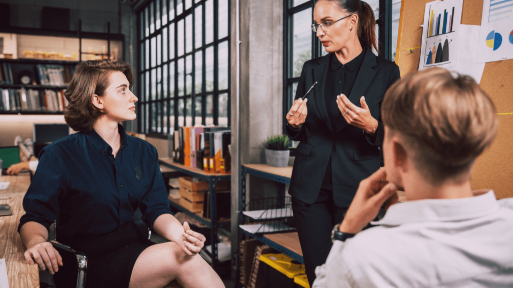 A woman stood up presenting during a meeting with a young man and young woman